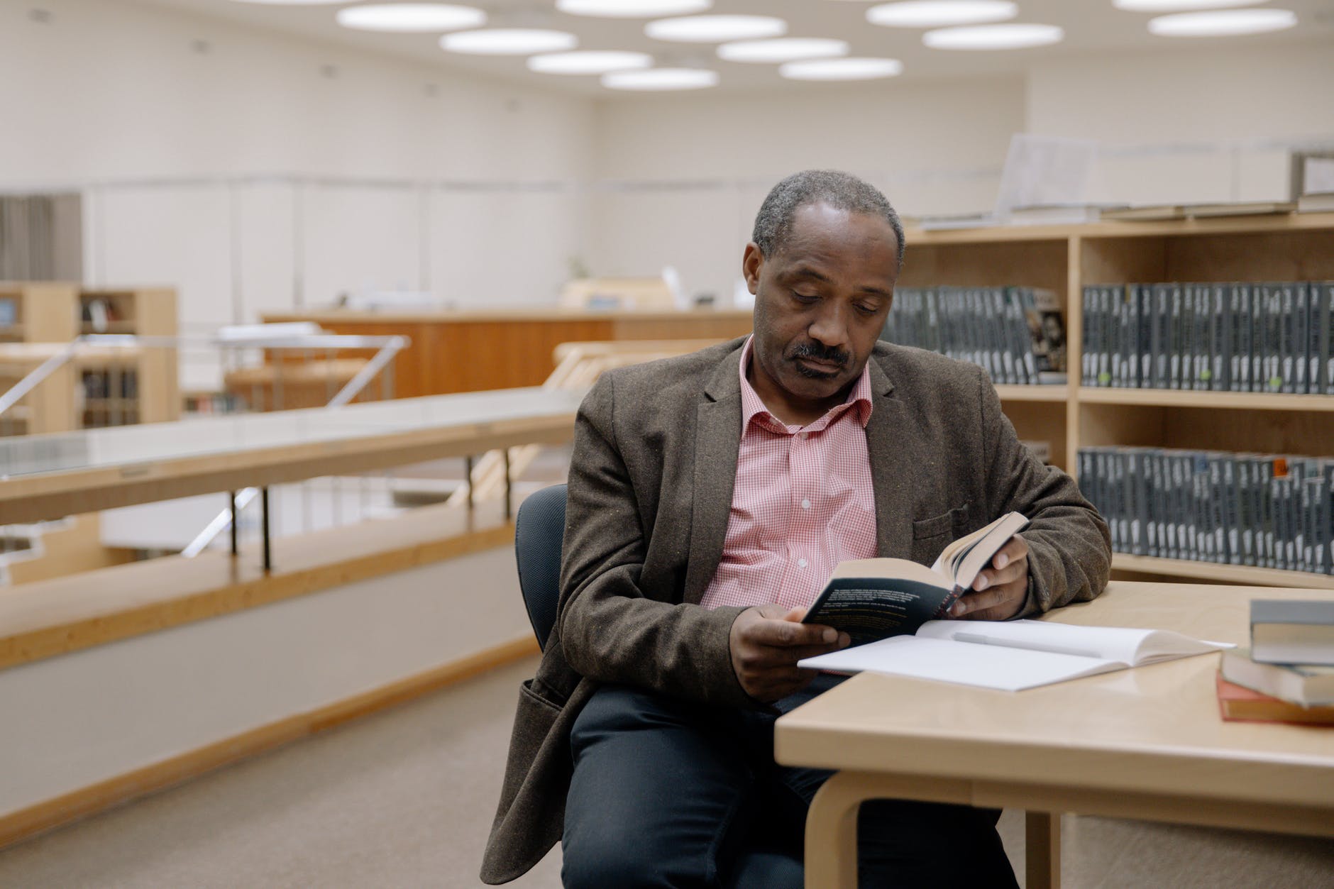 man in brown suit jacket sitting on chair reading a book