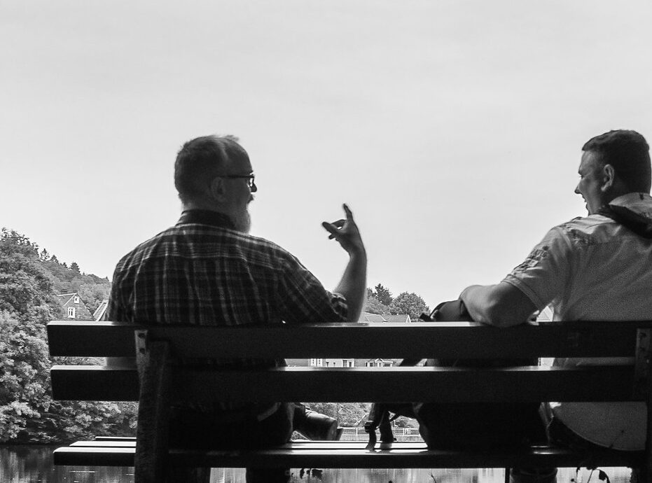 Two men sitting on a bench talking to each other.