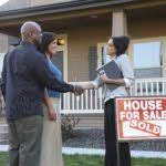 A couple of people shaking hands in front of a house.