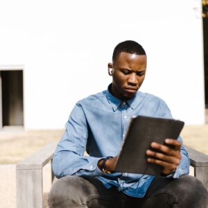 A man sitting on top of a bench looking at an ipad.